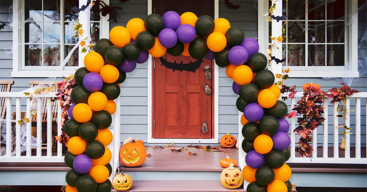 Halloween balloon arch in orange, black, and purple with jack-o’-lanterns on a decorated front porch.