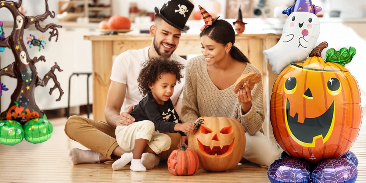 Smiling family carving pumpkins at home for Halloween, surrounded by festive balloon decorations including a spooky tree, ghost, and jack-o-lantern balloons.