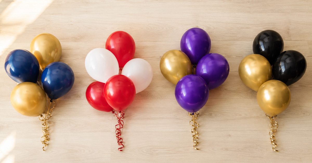 A variety of small balloon bouquet bundles for graduation party decorations displayed together on a light wooden background, showcasing different school color combinations.